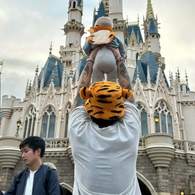 Bir baba ve bebeğin Disney kalesinin önünde başında kaplan desenli şapkalarla poz verdikleri eğlenceli bir an.