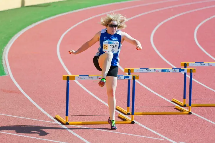 Güneşli bir günde, kırmızı bir atletizm pistinde bir engelin üzerinden atlayan, rüzgarda savrulan sarı saçları ve güneş gözlükleriyle genç bir kadın atletin enerjik anı, efsaneleşmiş Olimpiyat sporcularının sahip olduğu atletik yeteneği ve mücadeleci ruhu akıllara getiriyor.