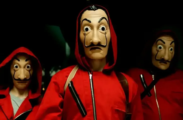 Kırmızı kapüşonlu tulumlar ve abartılı bıyıklarıyla tanınan Salvador Dalí maskeleri takan üç figürün karanlık bir arka plan önünde durduğu, sanatçının ikonik yüzünün kültürel etkisini veya eserlerine yapılan göndermeleri vurgulayan bir görsel.