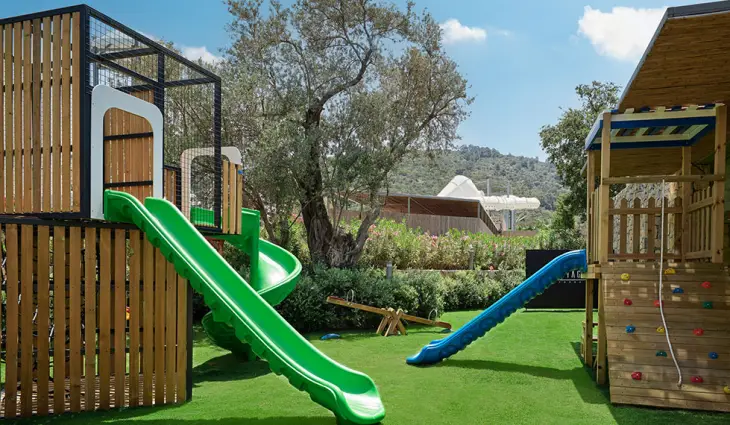 Marka Adı: Tugi Kids World
Ürün Adı: Tugi Kids World Çocuk Açık Hava Oyun Alanı
Ürün Cinsiyeti: Çocuk
Ürün Tipi: Çocuk Oyun Alanı
Ürün Sezonsallığı: Belirtilmemiş
Ürün Çeşidi: Eğlence Alanı
Ürün Özellikleri: Bu açık hava çocuk oyun alanı, dayanıklı ahşap ve metal strüktürleri, canlı yeşil ve mavi renklerdeki kaydırakları ile çocuklara güvenli ve eğlenceli bir ortam sunar. Tırmanma duvarı ve ipi gibi fiziksel aktivite alanları, denge oyunları için ahşap tahterevalli ile çocukların motor becerilerini geliştirmeye yardımcı olur. Oyun alanının zemini, düşmeleri yumuşatan sentetik çimle kaplıdır. Otel bünyesindeki Tugi Kids World mini kulübün bir parçası olan bu alan, çocuklara uzman eğitmenler eşliğinde eğitici ve eğlendirici aktiviteler sunarak, onların hayal güçlerini ve fiziksel gelişimlerini destekler.
Öne Çıkan Detaylar:
- Canlı renklerde çoklu kaydıraklar
- Ahşap ve metalden sağlam oyun strüktürleri
- Çocukların güvenliği için sentetik çim zemin
Kimler Kullanıyor?: Enerjisi yüksek, yeni şeyler keşfetmeye meraklı, açık havada oynamayı ve arkadaşlarıyla birlikte eğlenceli zaman geçirmeyi seven çocuklar ve onlara güvenli, eğitici bir ortam sunmak isteyen aileler için idealdir. Bu alan, hem fiziksel aktivitelerle enerjilerini atmak hem de yaratıcı oyunlarla hayal güçlerini geliştirmek isteyen küçük misafirler için tasarlandı.