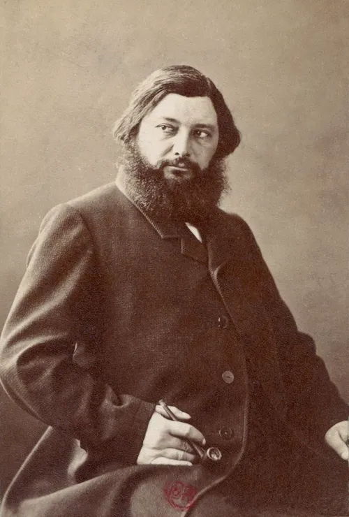 Sanatçı Gustave Courbet'nin koyu renk ceketli, gür sakallı ve uzun saçlı, sağ eliyle pipo tutarken hafifçe yana dönük, ciddi bir ifadeyle objektife baktığı sepya tonlu bir portre fotoğrafı.