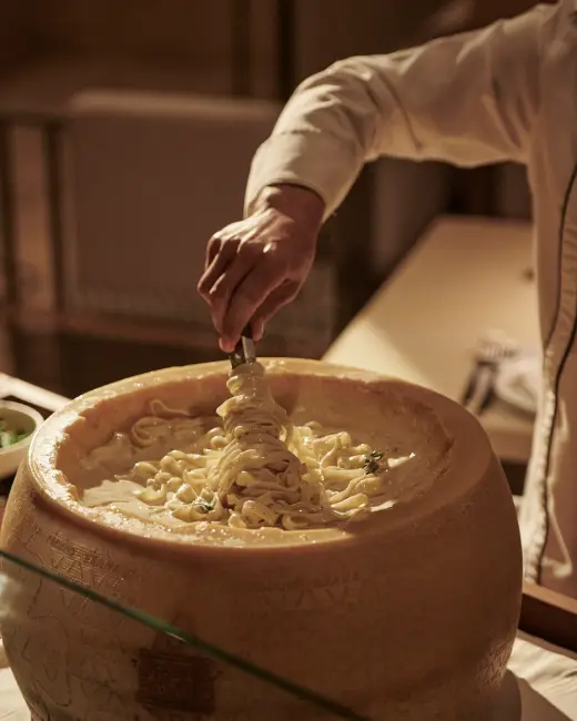 Bir şef büyük bir peynir tekerleğinin içindeki kremsi makarnayı maşayla karıştırarak servis ediyor, bu özel sunum Bodrum’un en iyi restoranlarındaki İtalyan ve dünya mutfağının zengin lezzet deneyimini gözler önüne seriyor.