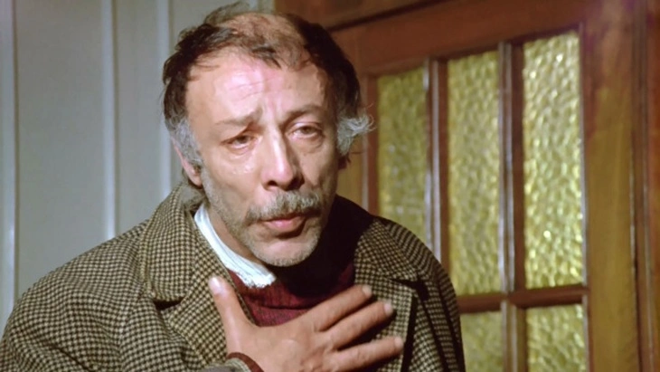 Bizim Aile filminden Münir Özkul'un canlandırdığı fedakar baba Yaşar Usta, ağlamaklı bir ifadeyle elini kalbine götürüyor.