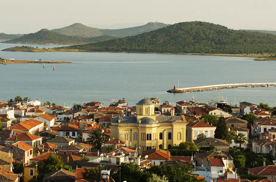 Ayvalık'ın tarihi dokusunu yansıtan, kırmızı kiremit çatılı eski Rum evlerinin ve görkemli Taksiyarhis Anıt Müzesi'nin öne çıktığı bir manzarada, Kuzey Ege'nin masmavi suları, yeşil adacıklar ve küçük teknelerin bağlı olduğu uzun bir iskele ile buluşuyor.