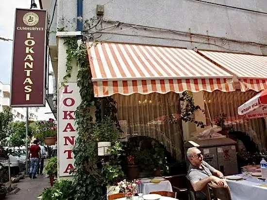 Edremit'in en iyi restoranları arasında yer alan Cumhuriyet Lokantası'nın kırmızı beyaz tentelerle gölgelenen dış cephesi, sarmaşıklarla çevrili sıcak atmosferi ve canlı şehir yaşamını yansıtan görünümü.