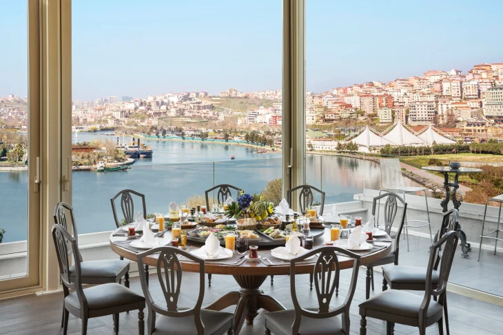 Işık alan şık bir teraslı mekânda, Jin Terrace'ın sunduğu Haliç'in geniş ve büyüleyici panoramik manzarasına karşı, çeşitli lezzetlerle donatılmış büyük yuvarlak bir yemek masası, etrafında oymalı detaylara sahip sandalyelerle birlikte keyifli bir deneyim vaat ediyor.