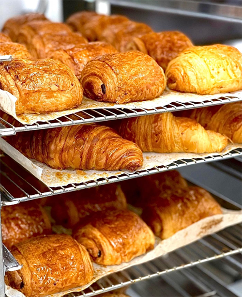 Tel raflarda, taze pişmiş, altın rengi, kat kat kruvasanlar ve çikolatalı çörekler sergilenirken, bu görüntü Paris'in en iyi pastanelerinde sunulan lezzetlerin ve şehrin gastronomik zenginliğinin cezbedici bir temsilini sunuyor.
