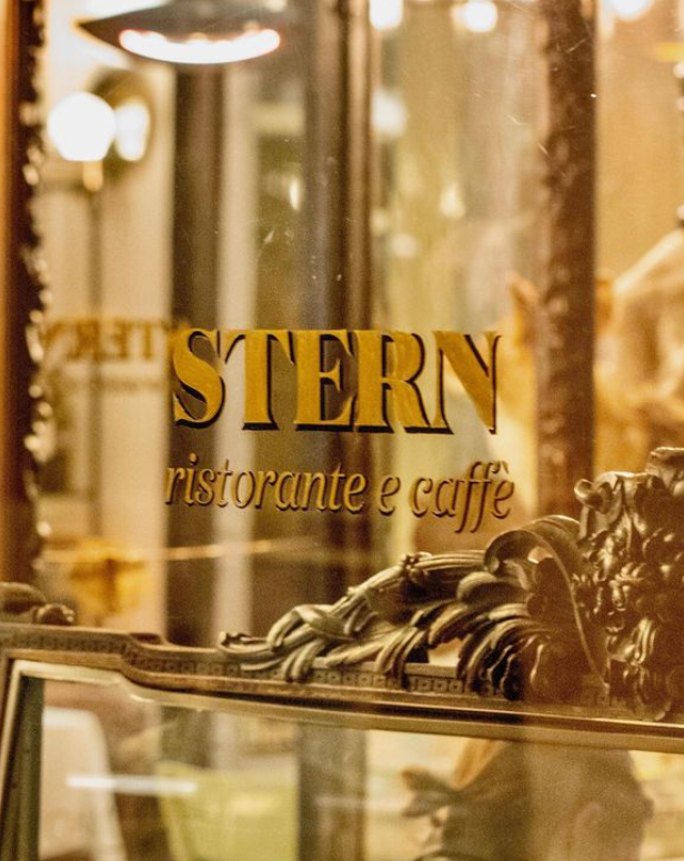 Paris'in en iyi restoranlarından biri olan Caffe Stern'in cam cephesinde altın harflerle STERN ristorante e caffè yazısı, alt kısmında ise geleneksel ve şık işlemeli koyu renk bir dekoratif unsur görünüyor.