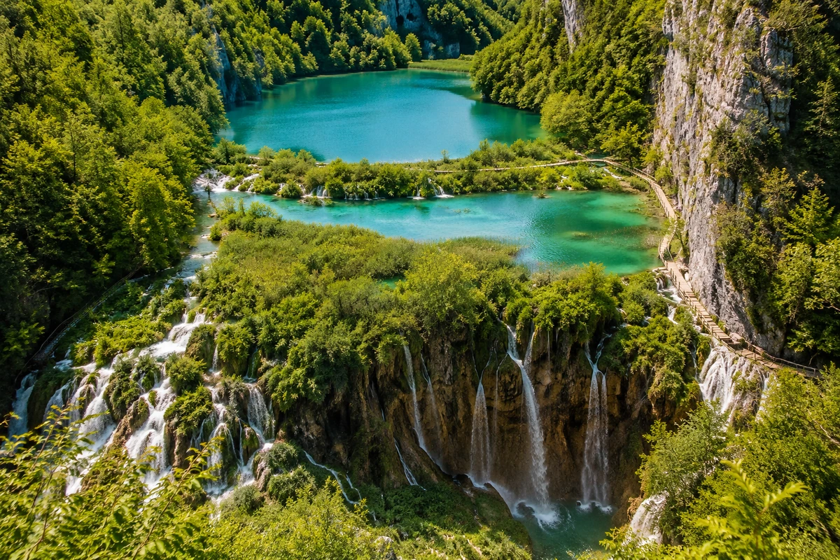 Hırvatistan'daki Plitvice Gölleri Milli Parkı'nın kuşbakışı görüntüsünde, yemyeşil ormanlarla çevrili turkuaz sulara sahip basamaklı göller ve görkemli şelaleler, ziyaretçilerin keşfedebileceği ahşap yürüyüş yollarıyla birbirine bağlanmış doğal bir cennet sunuyor.