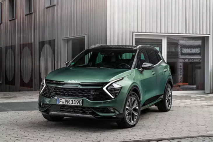 Yeşil Kia Sportage SUV, modern endüstriyel mimari önünde park halinde; dinamik ve çağdaş tasarımıyla öne çıkıyor.