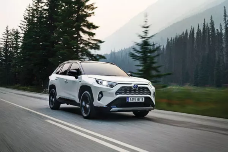 Beyaz Toyota RAV4 SUV, ormanlık dağ yolunda sürüş halinde; sağlam ve maceracı tasarımıyla öne çıkıyor.