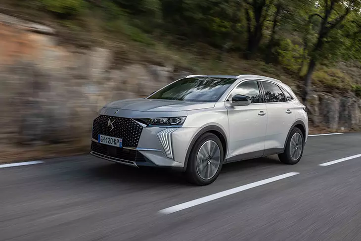 Gümüş DS 7 SUV, ağaçlık yol boyunca sürüş halinde; zarif ve modern tasarımıyla öne çıkıyor.