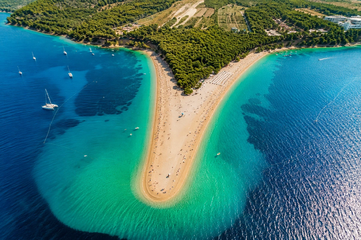 Zlatni Rat Plajı'nın havadan görünümü, turkuazdan koyu maviye uzanan Adriyatik Denizi'ne uzanan altın kumlu V şeklindeki burnu, güneşlenen insanları, yüzen tekneleri ve yemyeşil ağaçlarla kaplı kıyı şeridini çarpıcı bir şekilde gösteriyor.
