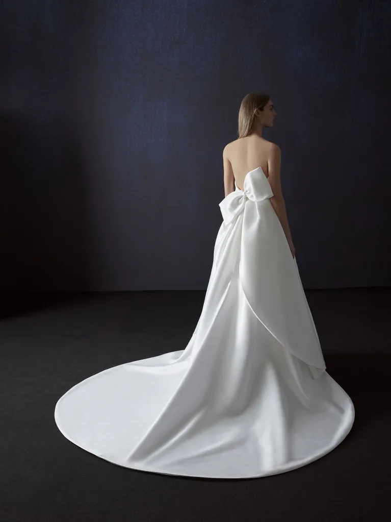 Atelier Pronovias tasarımı, uzun kuyruklu, sırt dekolteli ve büyük fiyonk detaylı straplez minimalist gelinlik.