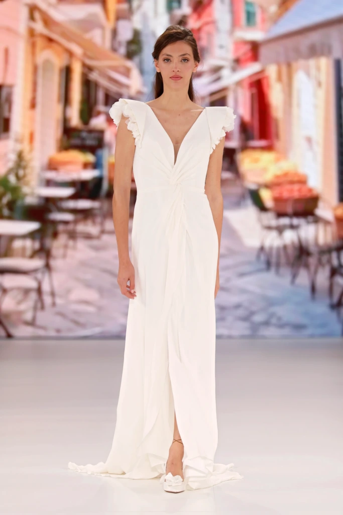 V yaka kesimli, omuzları fırfır detaylı, drape efektli ve akıcı kumaştan tasarlanmış Global Bridal House marka zarif gelinlik modeli.