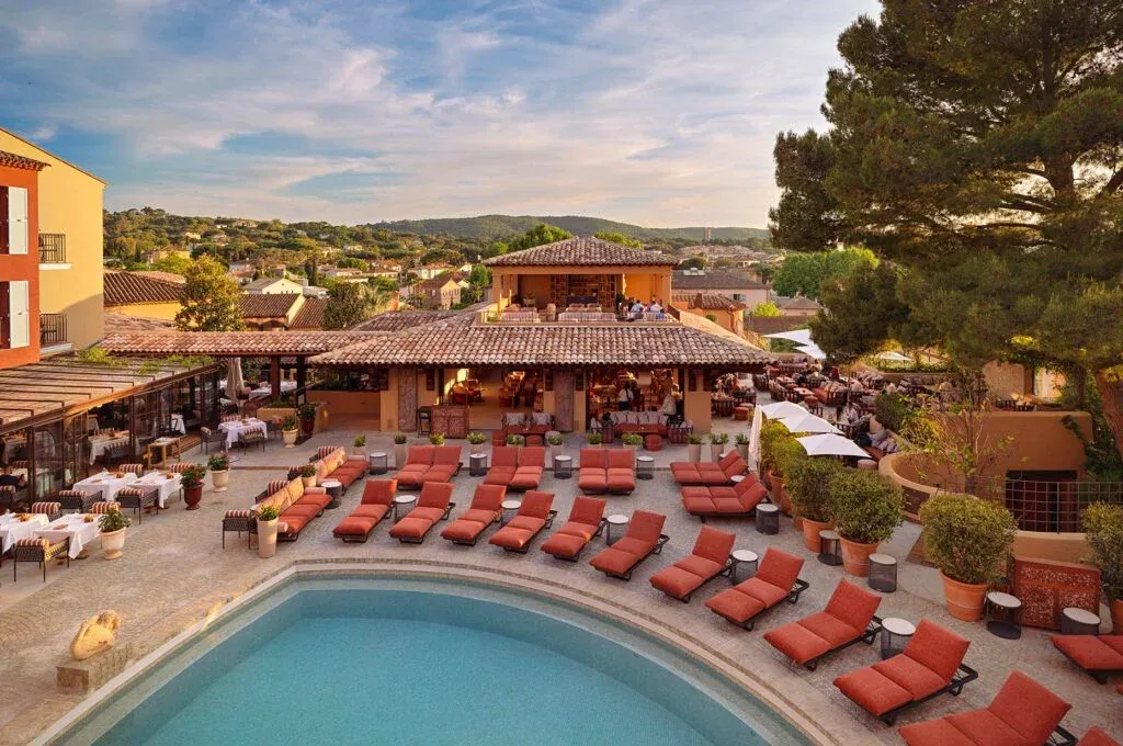 Hotel Byblos'un turkuaz yüzme havuzu etrafına sıralanmış turuncu şezlongları ve Akdeniz mimarisine sahip kiremit çatılı binaları, yemyeşil bitkilerle çevrili, tepedeki Saint-Tropez manzarasını sunan lüks bir Fransız Rivierası tatil atmosferini gözler önüne seriyor.
