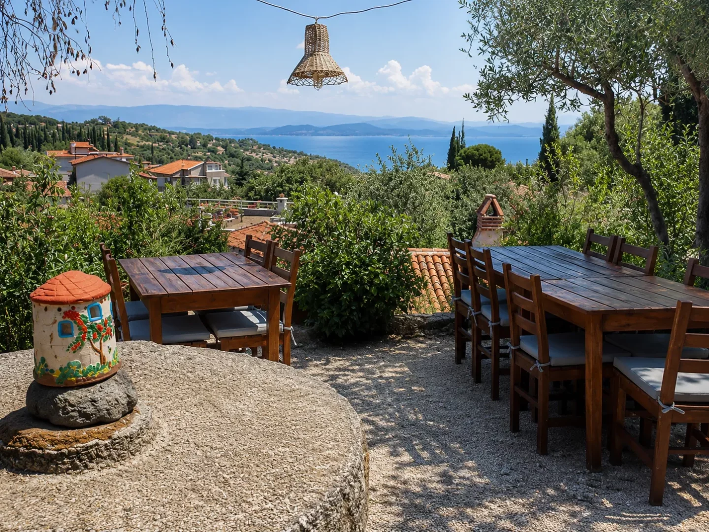 Kaz Dağları'nın doğal güzellikleri arasında, deniz ve uzak adalar manzarasına nazır bir otelin açık hava restoranı, zeytin ağaçlarının gölgesindeki ahşap masaları ve minderli sandalyeleriyle misafirlerine eşsiz ve huzurlu bir yemek deneyimi sunuyor.