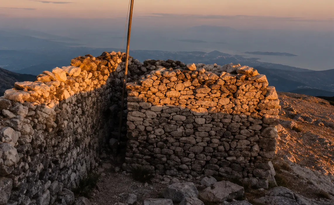 Kazdağları Sarıkız Tepesi'nde günbatımı veya gün doğumu ışıklarıyla aydınlanmış, taş duvarlardan oluşan eski bir yapının panoramik görüntüsü, arka planda uzanan sisli dağlar ve deniz manzarasıyla mistik bir atmosfer sunuyor.