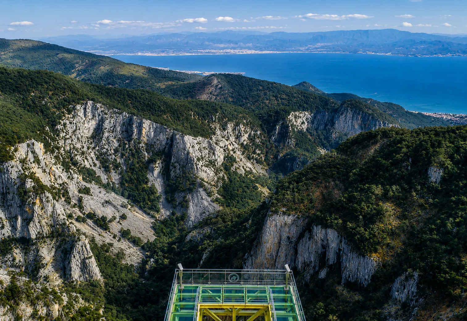 Ön planda duran, çevresini saran çam ağaçlarıyla kaplı dik kayalık yamaçları ve derin Şahindere Kanyonu'nu gözler önüne seren cam seyir terası, arka planda uzanan masmavi denizi ve uzak dağları net bir şekilde gösteriyor.