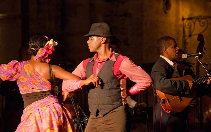 Küba’da geleneksel salsa dansı yapan çift ve canlı müzik eşliğinde performans sergileyen müzisyenler