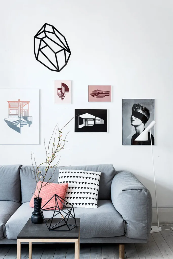 Geometrik sanat baskılarının yer aldığı beyaz duvar ve gri koltuk takımıyla dekore edilmiş genç ve çağdaş salon.