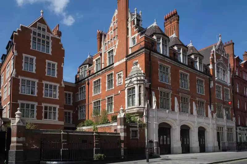 Chiltern Firehouse olarak bilinen, kırmızı tuğlalı, beyaz pervazlı pencereleri ve süslü sivri çatısıyla öne çıkan, zemin katında üç büyük kemerli girişi olan ikonik tarihi bina, masmavi gökyüzü altında dışarıdan çekilmiş geniş açılı bir fotoğrafta yer alıyor.