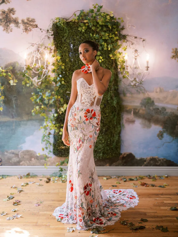 Claire Pettibone tasarımı, kırmızı ve yeşil tonlarda çiçek işlemeleriyle süslenmiş transparan ve straplez gelinlik modeli. Zarif silueti ve pastoral havasıyla rustik veya kır düğünleri için romantik ve sanatsal bir tercih sunuyor.
