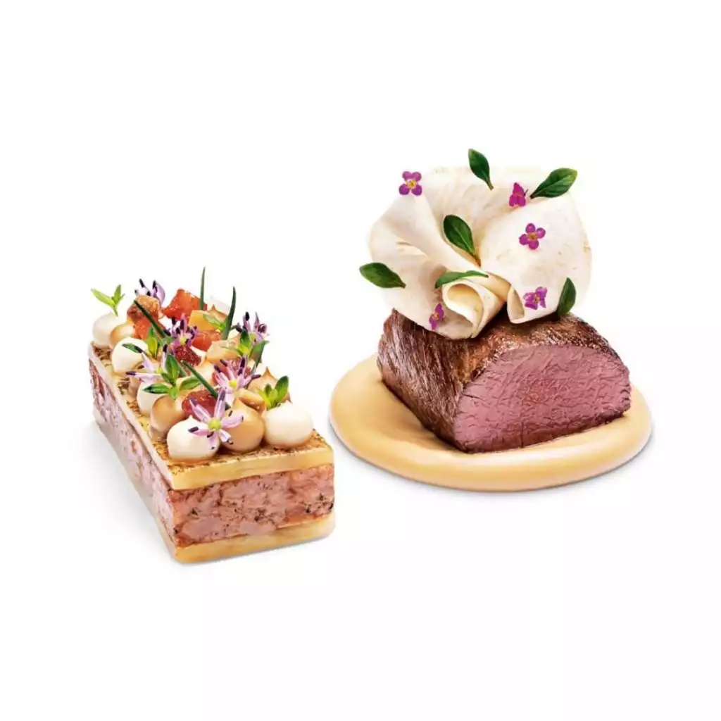 Core by Clare Smyth'in mutfağından çıkan, beyaz bir arka plan üzerinde sergilenen, biri mor çiçekler ve yeşil yapraklarla süslü katmanlı bir terrin, diğeri ise açık renkli bir sos üzerinde duran ve üzerinde yine çiçekler ve yapraklar bulunan narince pişirilmiş pembe renkli bir et yemeği olmak üzere iki ayrı sanat eseri gibi duran gurme tabak.