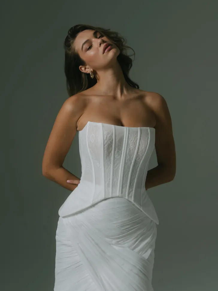 Hera Couture tasarımı, dantel dokulu straplez korse ve drapeli etek detaylarıyla dikkat çeken modern gelinlik modeli. Heykelsi bir form ve zarif bir romantizm taşıyan bu tasarım, güçlü bir siluet sunuyor.