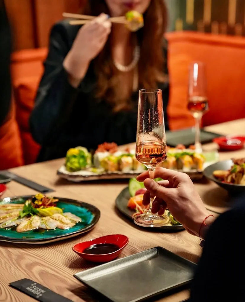Bir kadın İstanbul'un popüler sushi restoranlarından biri olan Sushi Manga'da masadaki çeşitli taze ve özenle hazırlanmış sushi roll'larından, levrek carpaccio'sundan ve özel soslardan tadarken, yakındaki bir el şık bir kadehte pembe şarabı tutarak bu modern Uzak Doğu deneyiminin keyfini çıkarıyor.