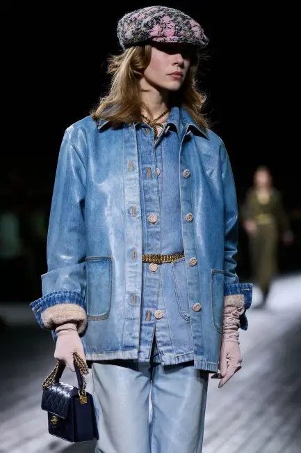 Bir defilede, açık mavi denim ceketi, ona uygun gömlek ve pantolonu, pembe eldivenleri, desenli şapkası ve küçük lacivert çantasıyla, kurumsal hayatta rahatlığın şıklıkla harmanlandığı casual giyim koduna örnek oluşturan özgün ve etkili bir stil sergileyen bir model.