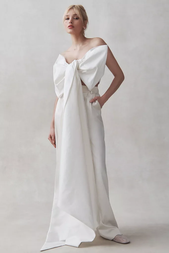 Omuzları açıkta bırakan ve gövde kısmında büyük bir fiyonk detayına sahip bu beyaz bridal tasarım, modern, zarif ve beklenmedik bir silüet yaratıyor.