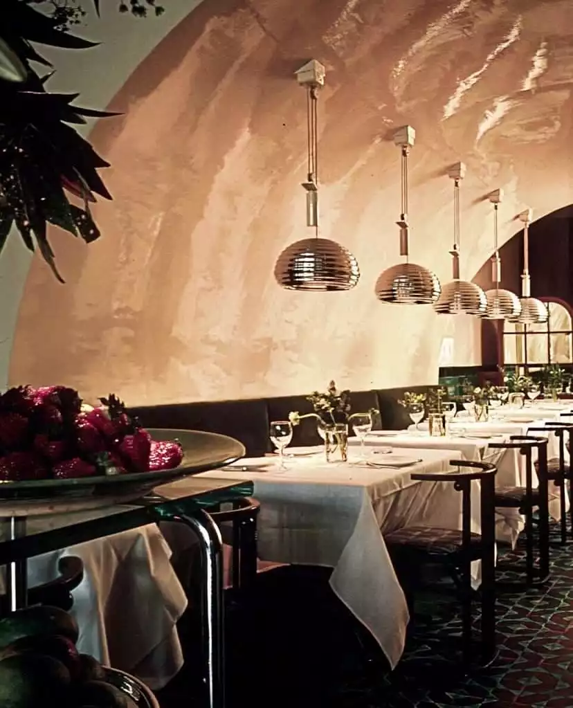 Mr. Chow restoranının kemerli tavanı ve dalgalı dokulu duvarlara sahip şık iç mekanında, tavandan sıra halinde asılı duran metalik sarkıt lambaların aydınlattığı, beyaz örtülü uzun masalar özenle hazırlanmış olup, sol önde parlak kırmızı çileklerle dolu büyük bir servis tabağı göze çarpıyor.