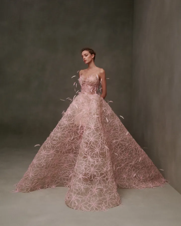Pudra tonlarında, üç boyutlu floral aplikelerle kaplanmış straplez balo tipi gelinlik modeli. Nicole + Felicia imzalı bu gösterişli tasarım, couture ihtişamı ve modern zarafeti bir arada sunuyor.