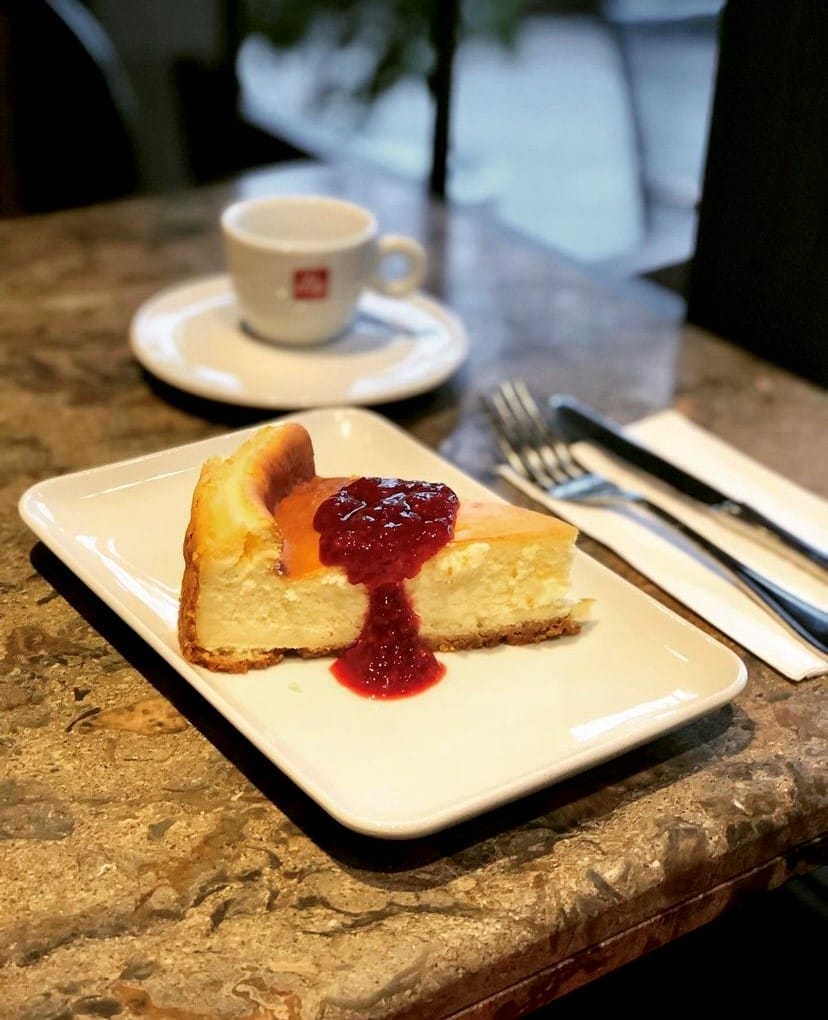 Mermer yüzeyli bir masada, üzerinde parlak kırmızı, akışkan meyve sosuyla zenginleştirilmiş, fırınlanmış, kremamsı dokuya sahip cazip bir dilim cheesecake, küçük bir kahve fincanı ve çatal bıçak takımı eşliğinde sunularak, Etiler ve Akatlar'daki gurme lezzet duraklarının vazgeçilmez tatlı seçeneklerinden birini gözler önüne seriyor.