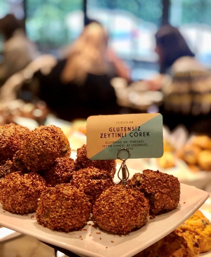 All Sports Bakery'de sunulan, üzerinde bolca susam bulunan ve glütensiz un, zeytin ezmesi, ay çekirdeği ile ceviz içeren bu zeytinli çörekler, Etiler ve Akatlar'ın sağlıklı ve gurme lezzet durakları arasında mutlaka denenmesi gereken bir seçenek olarak öne çıkıyor.