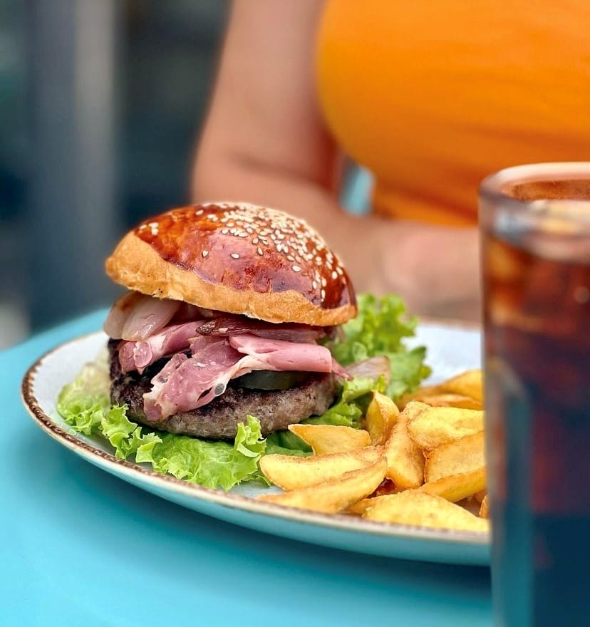 Parlak mavi bir masada, susamlı ekmeği, kalın köftesi, taze marulu, turşusu ve bol tütsülenmiş et dilimleriyle iştah açıcı görünen bir hamburger tabağı, yanında altın sarısı çıtır patates kızartmaları ve koyu renkli bir içecek ile birlikte Etiler'in en sevilen mekanlarındaki lezzetli seçenekleri sunuyor.