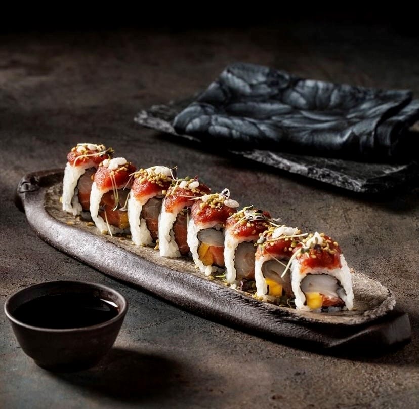 Koyu renkli rustik bir tabakta özenle dizilmiş sekiz adet sushi rulosu, içindeki balık ve mango dilimleri, üzerindeki nar gibi kırmızı ton balığı tartarı ve taze filizleriyle Inari Sushi Omakase'nin Uzak Doğu mutfağından sunduğu estetik lezzetleri yansıtırken, yanında soya sosuyla birlikte Etiler'in seçkin mekanları arasında kendine yer buluyor.