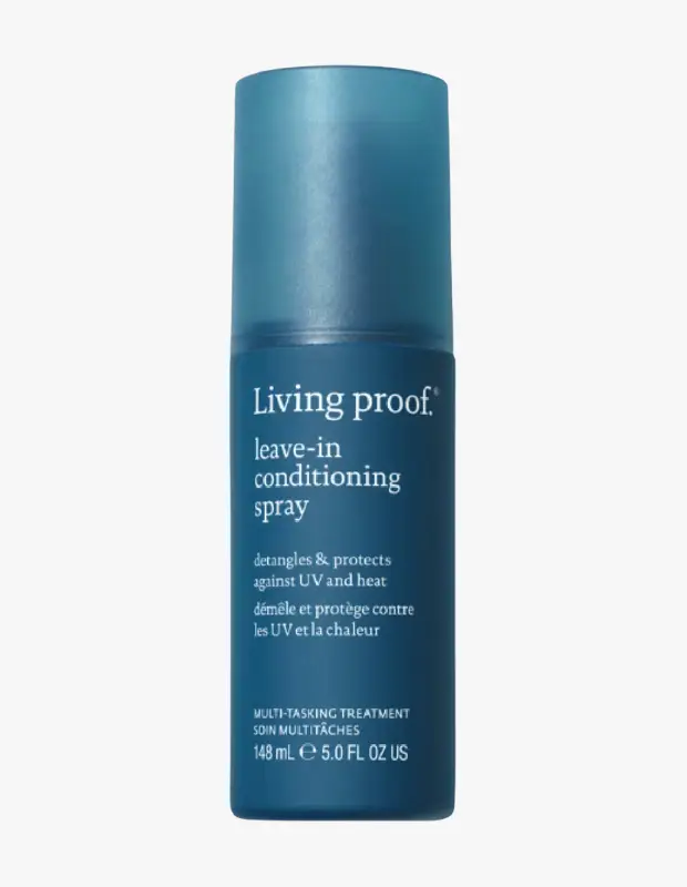 Living Proof markasının şeffaf açık mavi kapaklı, koyu mavi renkli, üzerinde Living Proof leave-in conditioning spray yazan saç spreyi şişesi beyaz bir arka plan üzerinde dik bir şekilde duruyor, saçları UV ışınlarına ve ısıya karşı koruyan bu çok görevli ürün düğümleri açmaya da yardımcı oluyor.