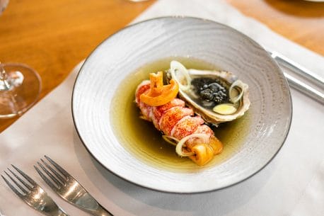 Bir Selanik restoranında özenle sunulan bu fotoğraf, parlak kırmızı ıstakoz veya kerevit kuyruğu, siyah havyarla süslenmiş taze bir istiridye ve berrak, aromatik sosuyla beyaz bir tabakta zarifçe düzenlenmiş, şehrin gastronomi kalitesini yansıtan nefis bir deniz ürünü tabağını gözler önüne seriyor.