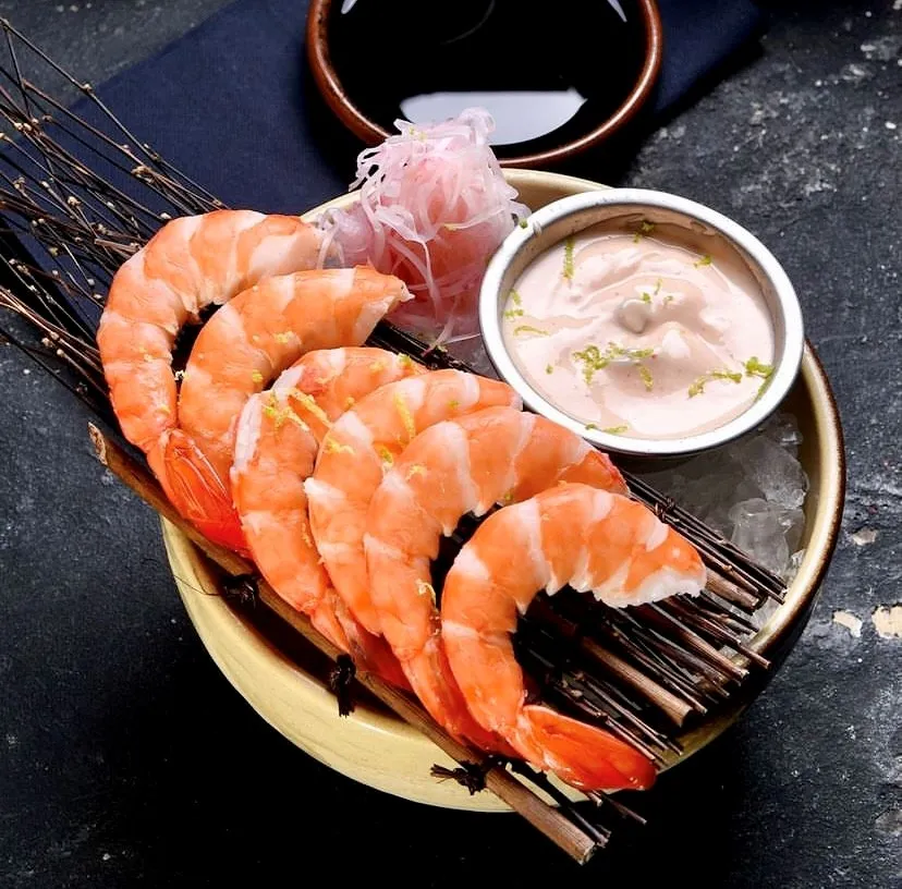 İstanbul'un en iyi sushi restoranlarından birinde sunulan, kuru otlar üzerinde buzla sergilenen limon zestli taze haşlanmış karidesler, özel kremsi sosu ve hafif pembe turşu garnitürüyle Uzak Doğu mutfağının rafine deniz mahsulleri sunumunu yansıtıyor.