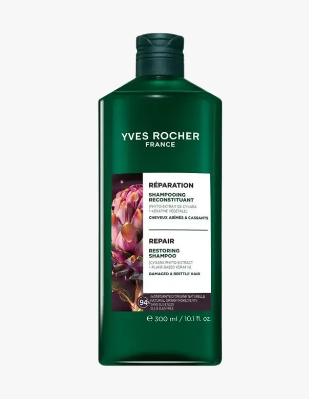 Düz beyaz bir zeminde dikey duran, Yves Rocher markalı koyu yeşil bir şişe; etiketinde mor enginar çiçeği görseli, hasarlı ve yıpranmış saçlar için Bitkisel Keratin içeren 300 ml Onarıcı Şampuan ibaresi yer alıyor.