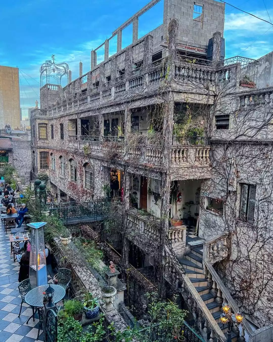 San Telmo'da yoğun sarmaşıklarla kaplı tarihi bir binanın katmanlı cephesinde, demir korkuluklu balkonlar ve açık havada oturan insanların görüldüğü Atis Bar, Buenos Aires'in bohem atmosferini yansıtan büyüleyici bir kokteyl durağı.