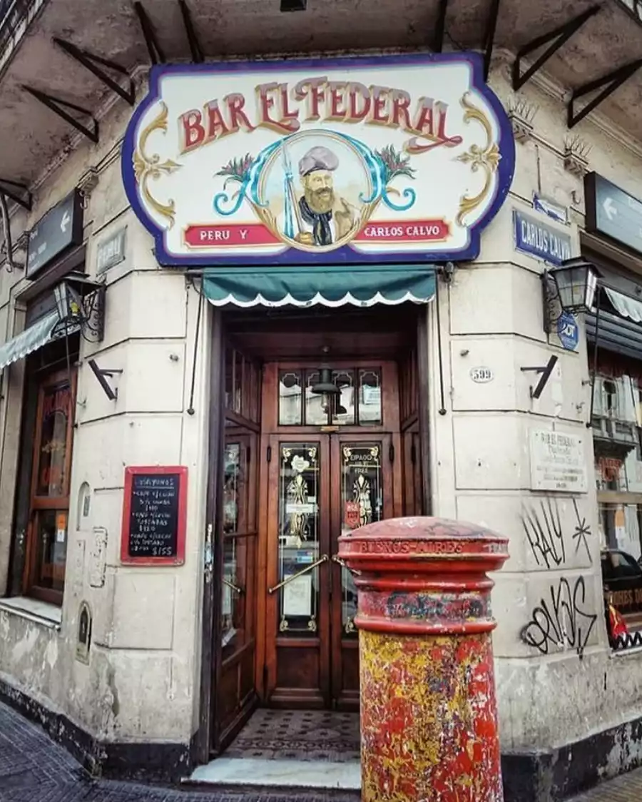 Buenos Aires'in tarihi San Telmo bölgesinde yer alan, ahşap detaylı oymalı kapısı ve üzerinde Gaucho figürü bulunan Bar El Federal tabelasıyla nostaljik bir köşe oluşturan bu mekan, şehrin otantik ruhunu ve tutkusunu yansıtan ikonik bir buluşma noktasıdır.
