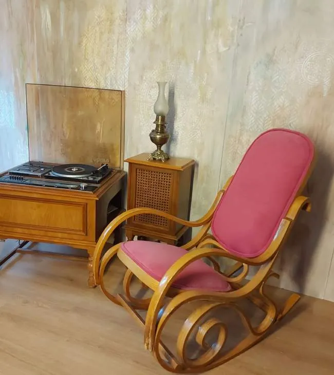 Eski model ahşap pikaplı konsol, antika bir gaz lambası ve pembe minderli ahşap sallanan sandalye bir arada sunulmuş, retro bohem düğün dekorasyonu için ilham verici bir köşe.