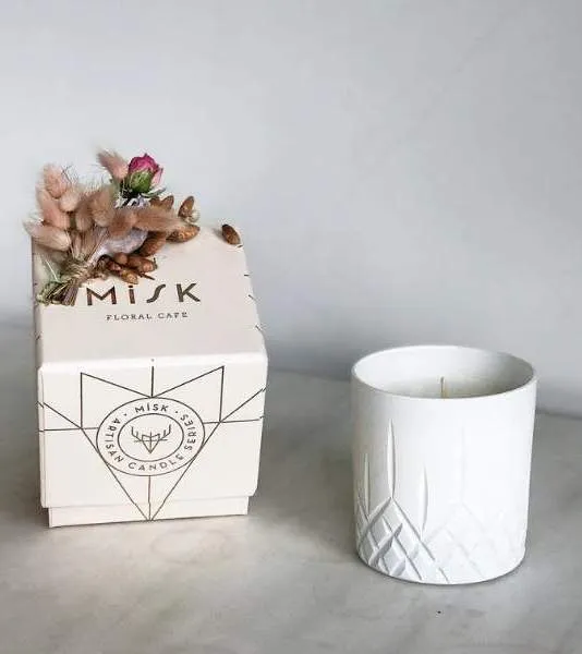 Misk Floral Cafe’ye ait şık tasarımlı kutu ve yanında beyaz seramik mum; üzerinde kuru çiçek detaylarıyla estetik bir sunum.