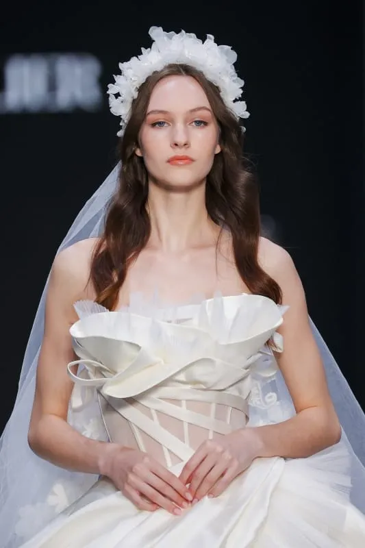 Beyaz tül çiçeklerden oluşan hacimli taç ve romantik kesimli gelinlik giyen model. Boho gelin stiline teatral ama zarif bir yorum katıyor.