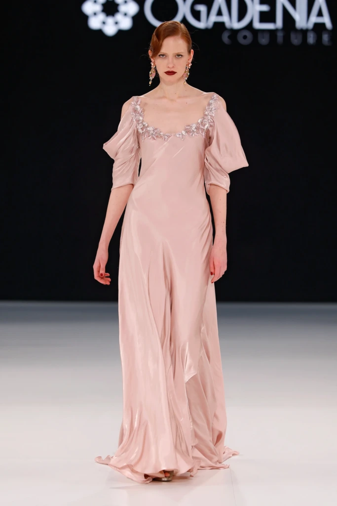 Soluk pembe ipeksi dokusuyla zarafeti yansıtan Ogadenia Couture tasarımı gelinlik. Omuz detayı ve çiçek nakışlarıyla modern romantizmi yansıtıyor.