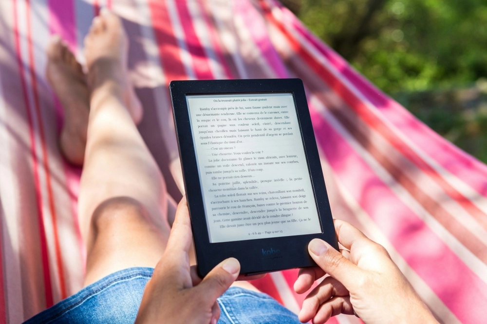Güneşli bir günde pembe çizgili bir hamakta uzanmış, kot şortlu bir kişinin ellerinde Kobo e-kitap okuyucusuyla keyifli bir şekilde Fransızca bir kitap okuduğu, bacaklarının rahatça uzandığı görülüyor.