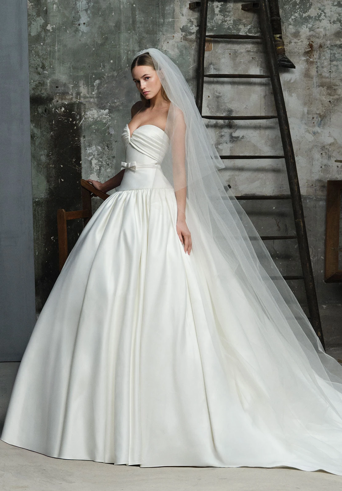 Drapeli straplez üst, fiyonklu bel detayı ve kabarık etekli Elie Saab gelinlik; uzun duvakla tamamlanan zamansız bir bridal stil.